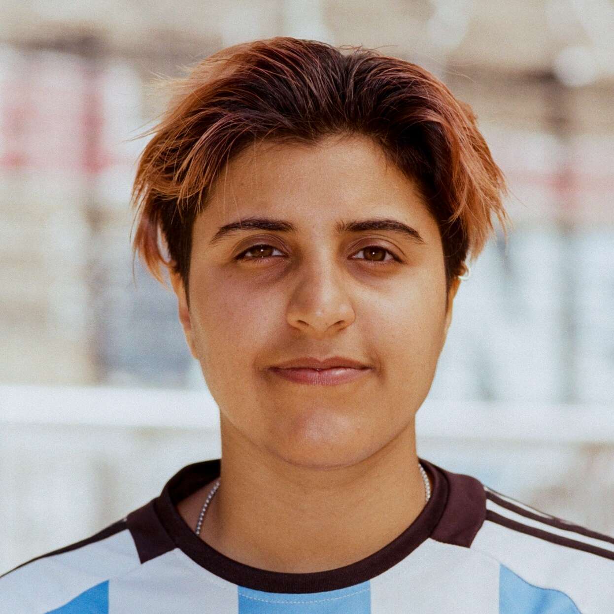 Eine junge Frau mit kurzen Haaren in einem Fußballtrikot blickt in die Kamera.