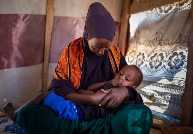 Halima holds her young child in her arms in a tent at a camp for internally displaced people in Somalia.