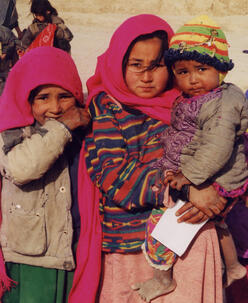 밝은 분홍색 옷을 입은 세 명의 젊은 아프간 소녀들이 사진을 찍기 위해 포즈를 취하고 있습니다.
