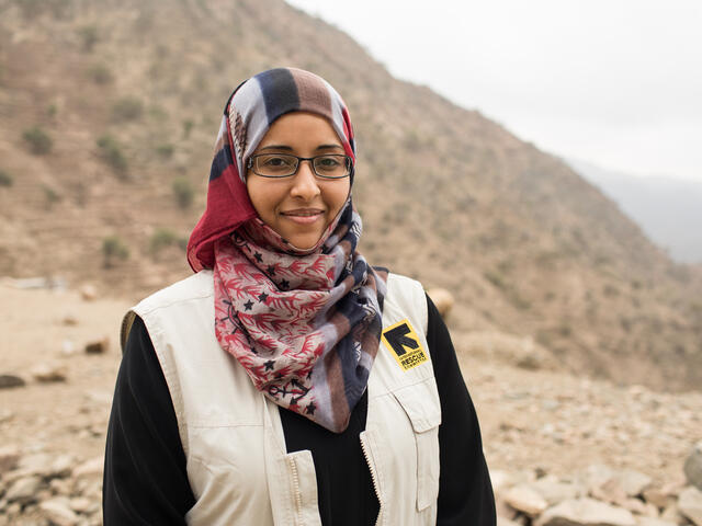Dr Rasha Rashed, wearing an IRC vest, stands outside in front of a desert landscape