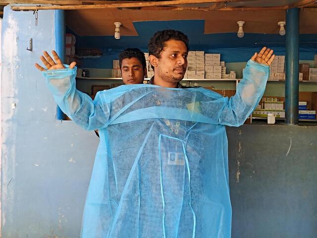 Dr, Mahmudul Hossain stands in front of a group of health care workers and volunteers and demonstrates how to correctly put on a medical gown. 
