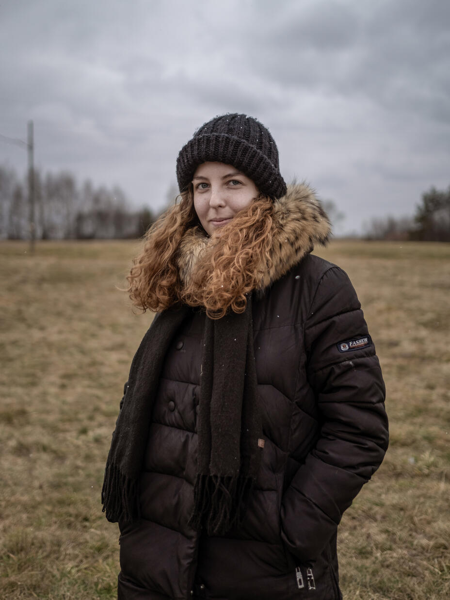 A portrait of Anastasiia in a field, wearing a winter coat and hat. 