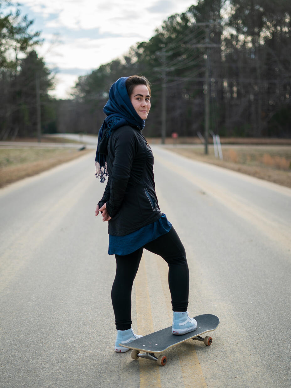 A young woman on a skateboard on the road looks at the camera 