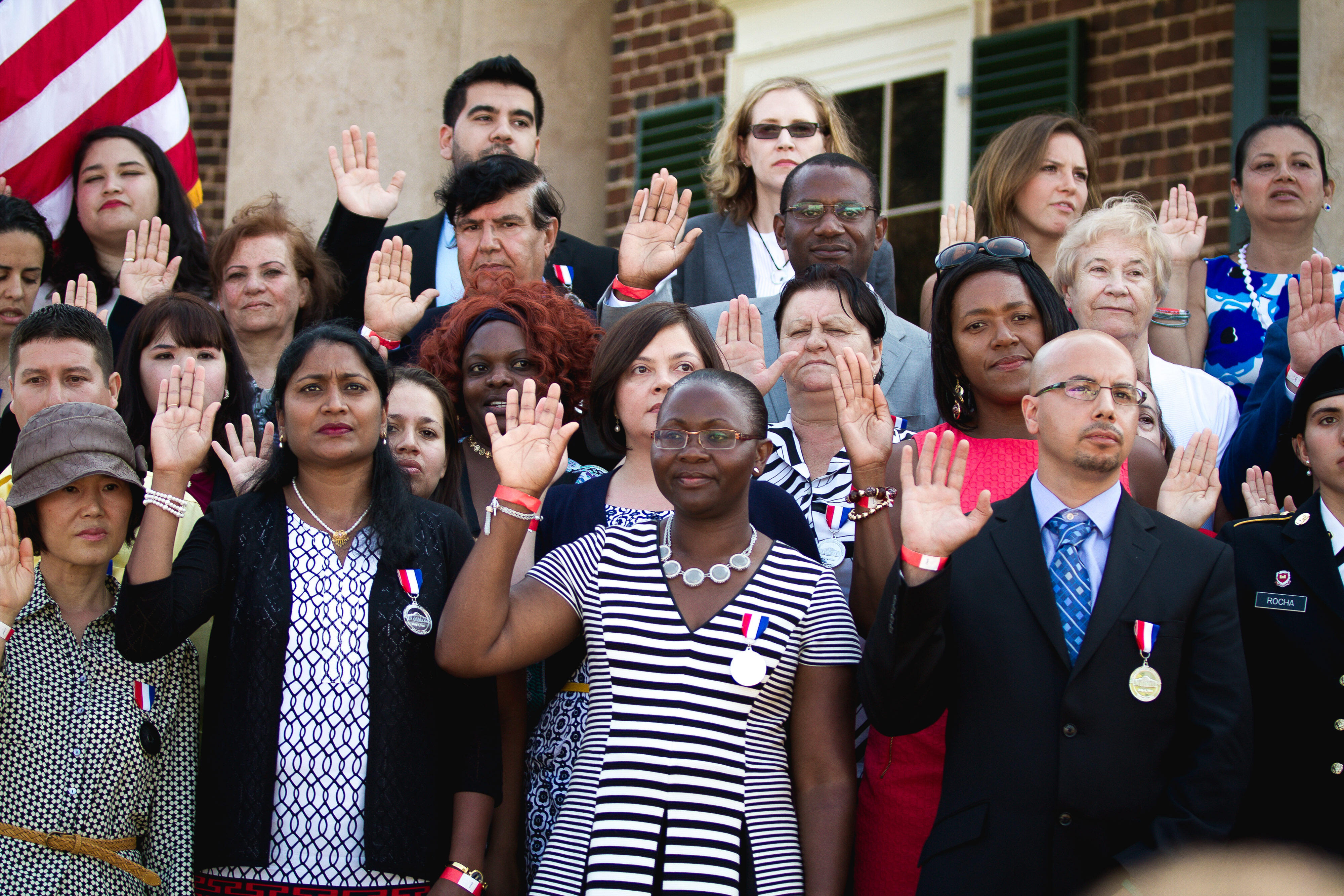 Group of people resettled in the U.S. stand together and raise their right hands as they are sworn in as citizens.