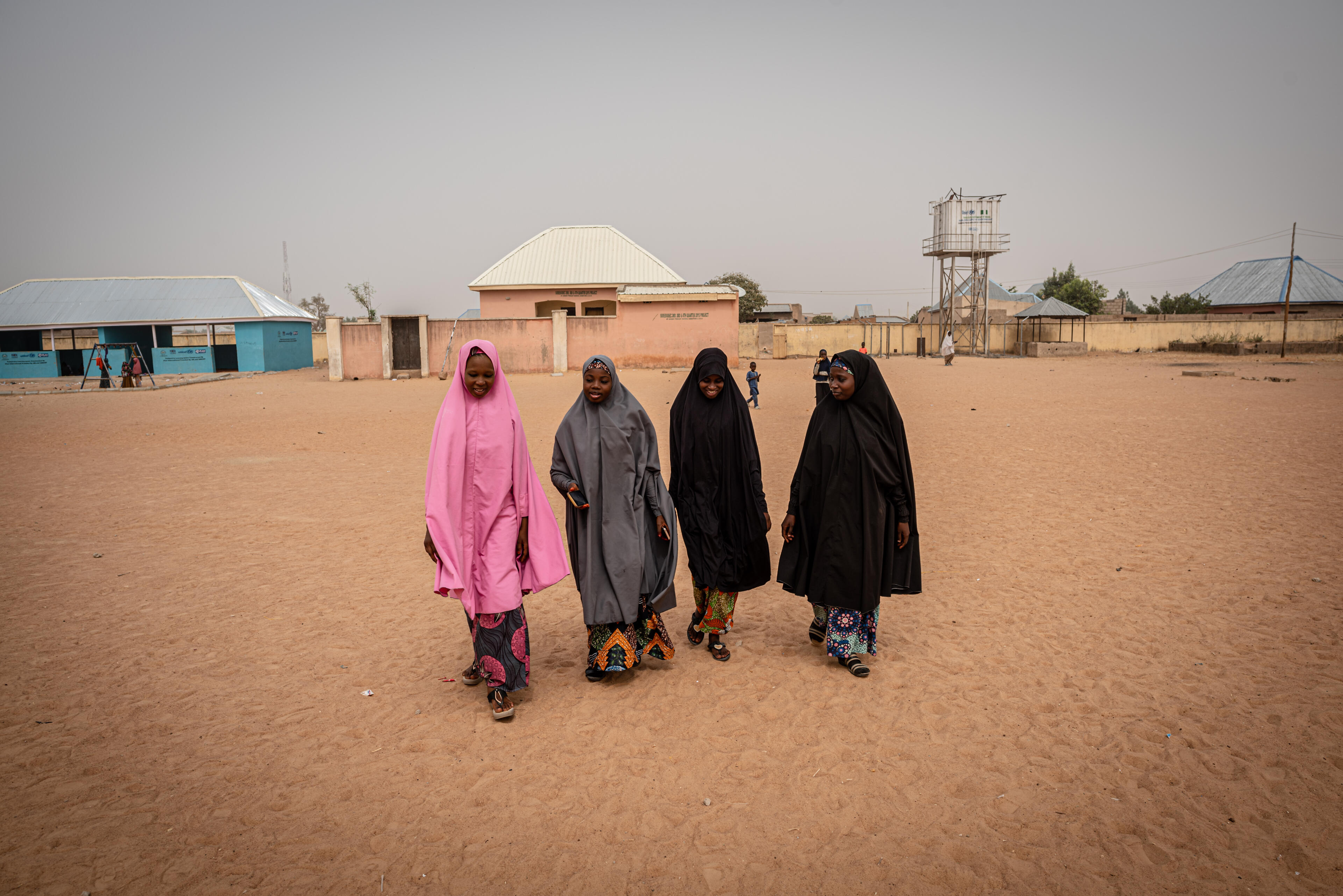17-year-old Hauwa and four of her friends walk in a straight line across sandy soil near an IRC safe space in Niheria