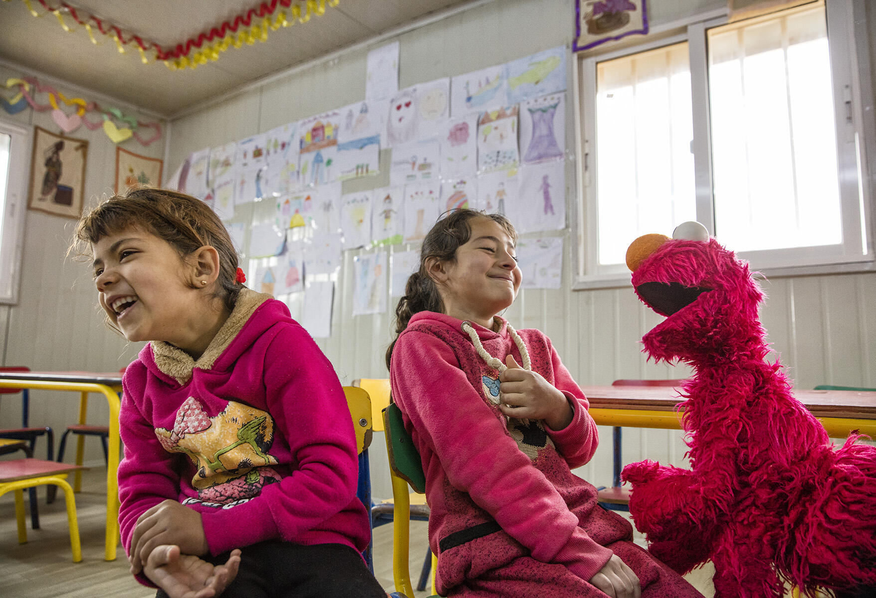 Two Syrian girls laugh as they play with Sesame Street Muppet Elmo 