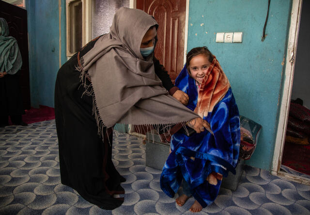 Outside of their home in Kabul, Afghanistan, a mother wraps her smiling daughter in a new blanket.
