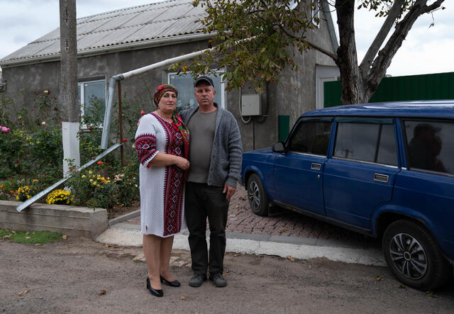 Olga poses for a photo next to her husband in front of their home in Ukraine. Although their home is in good condition, war has severely impacted their community and forced the pair to take shelter underground for extended periods of time.