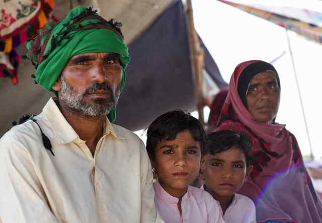 파키스탄에서 2022년 홍수가 발생한 후 파르자나, 굴람과 그들의 두 아이들이 임시 대피소 아래 앉아 있습니다.