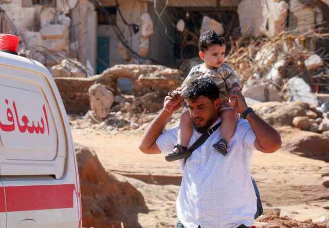 A man holds a boy high on his shoulder while walking through Derna, Libya after the flooding.