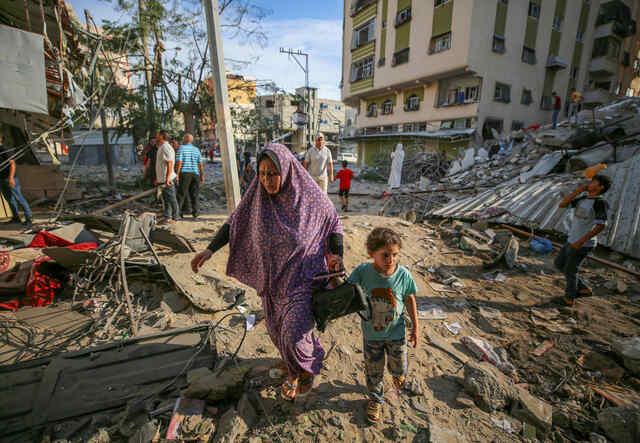 En mamma går med sitt barn genom ruinerna efter israeliska luftangrepp i Gaza den 7 oktober 2023.