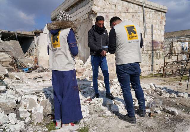 Två av RESCUE:s medarbetare delar ut kontantstöd till en person framför ett raserat hus efter jordbävningen i Turkiet och Syrien. 