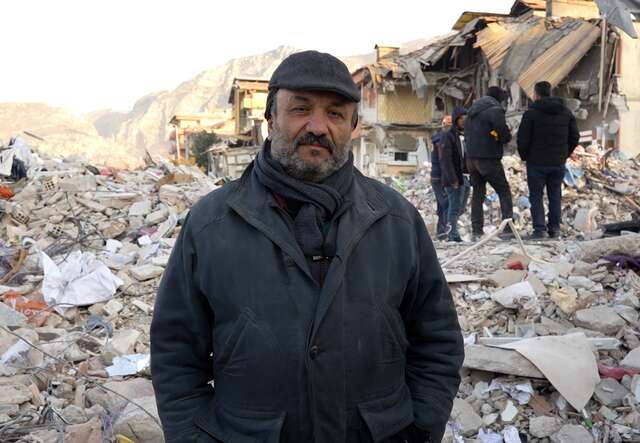 Kahit poses for a photo in front of buildings destroyed in the Syria-Turkey earthquake.