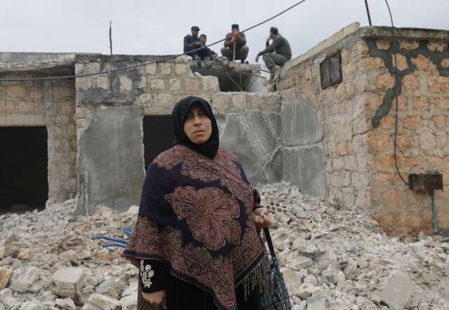En kvinna står framför ett raserat hus efter jordbävningen i nordvästra Syrien.