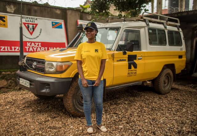 A female IRC staff member stands in front of an IRC-branded vehicle in the DRC.
