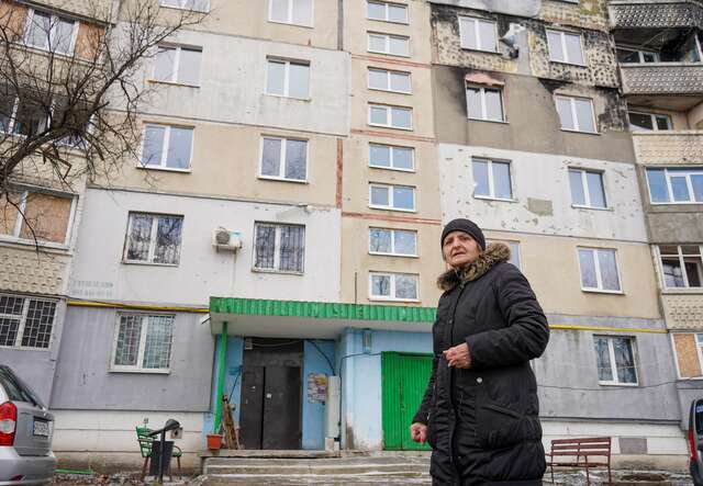 Kateryna stands in front of her apartment in Ukraine, which shows shelling damage