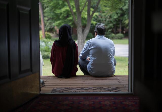 In a doorway to a home, a couple sits on a stoop and looks away from the camera. 