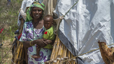 A displaced mother, smiling, holds her baby boy outside a makeshift tent in northern Cameroon.