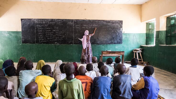 International Rescue Committee teacher Fatima writes on a blackboard in the front of her classroom.