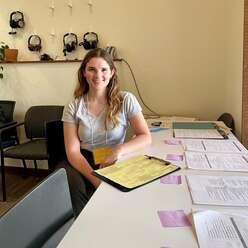 A woman sits at a desk with a variety of tax forms in front of her.