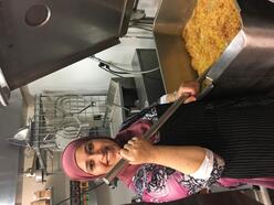 A woman with a hijab smiling frying something in a commercial kitchen. 