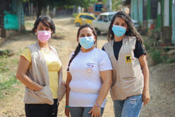 Omaira and two other IRC volunteers smiling for a photo outside of a volunteer site.