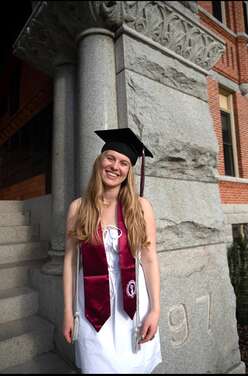 A woman stands against a stone column wearing a University of Montana stole