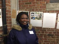 Leonia, gardener with New Roots, standing in front of her photographs.