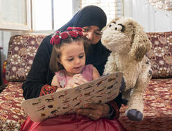 A child learns her letters and numbers alongside her caregiver and Ma’zooza, a new character from the Ahlan Simsim TV show.