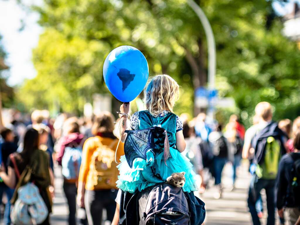 Inmitten eines Protests hält ein Kind einen Luftballon mit einer Weltkarte hoch.