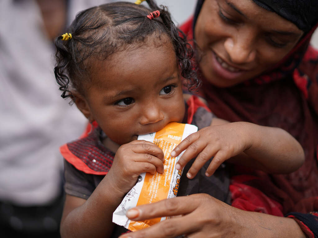 En 3-årig flicka i Jemen äter nötkräm som RESCUE delar ut.
