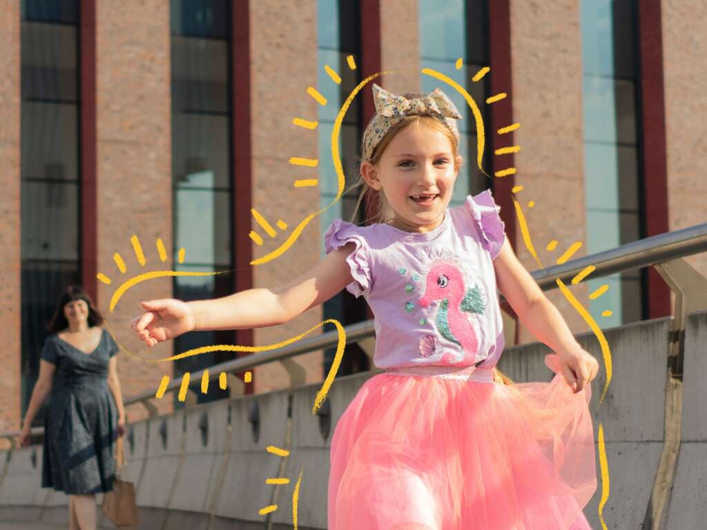 A girl, wearing a pink dress, plays outside.