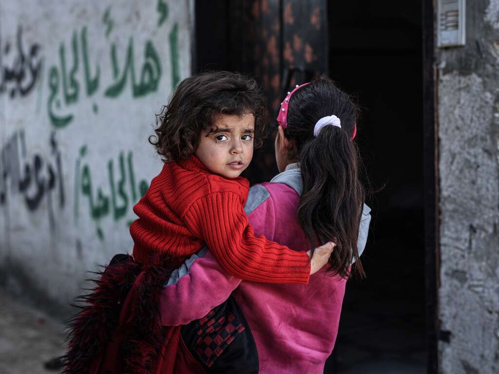 A mother carries her young child on her shoulder. The child looks towards the camera.