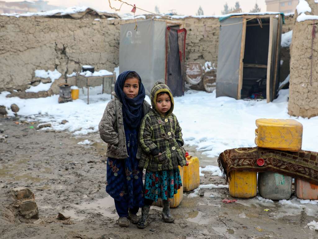 Two children stand in snow outside their home