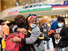 A refugee family is reunited at an American airport. The family hug each other in a warm embrace and smile.