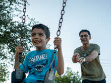 A man pushes a boy in a swing.