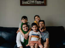 A family sits together on a couch and poses for a photo.