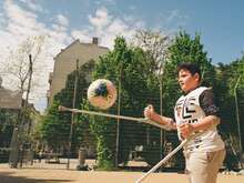 Ein Junge auf Krücken spielt Fußball auf einem sonnigen Spielplatz, konzentriert den Ball mit seinen Krücken jonglierend.