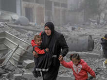 A mother holds her two children while she makes her way through the remnants of a building destroyed by the war in Gaza.