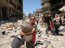 A young girl holds a blanket while walking the ruins of a street in Gaza.