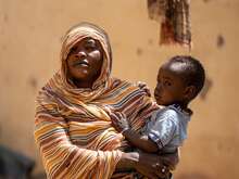 Woman holding a child against backdrop of destroyed building