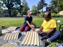 Two people sitting outdoors making items from bamboo.