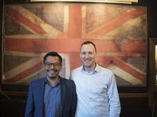 Two men standing in front of a large Union Jack flag.