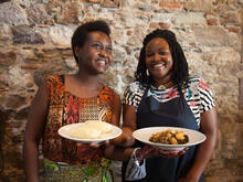 Two women holding a plate of spinach and tuna with African fufu.