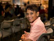 Syrian boy sitting in chair, smiling, at a UN Refugee Event in Los Angeles