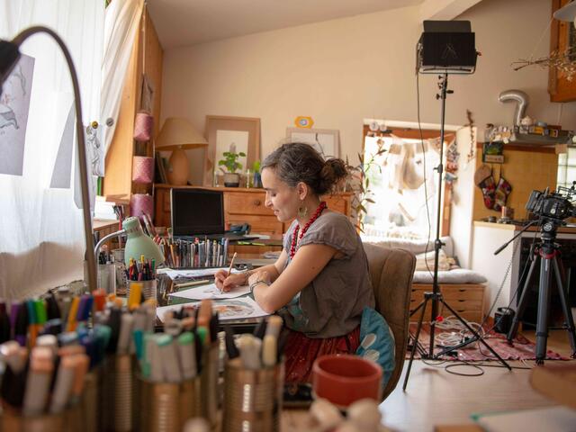 Diala sits at her desk and paints