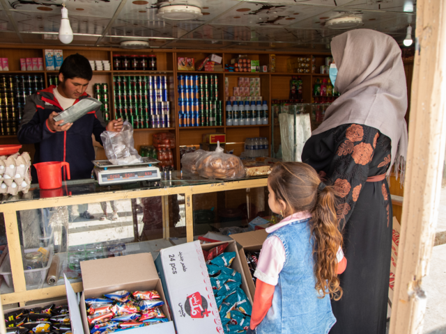 Noor holds her daughters hand while standing at a market.