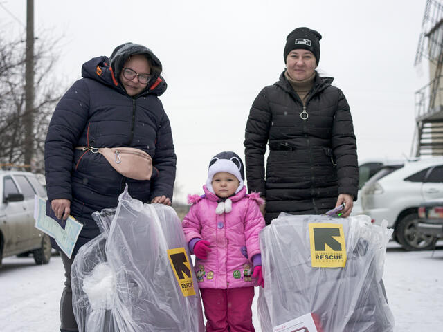 Two women and a small girl holding bags of supplies from the IRC