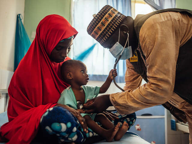 En kvinna i Nigeria håller ett litet barn i famnen samtidigt som en läkare underösker barnet. 