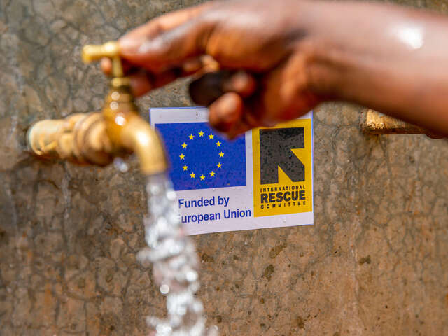 Ein Wasserhahn mit frischem Wasser, im Hintergrund die Logos von EU und IRC.
